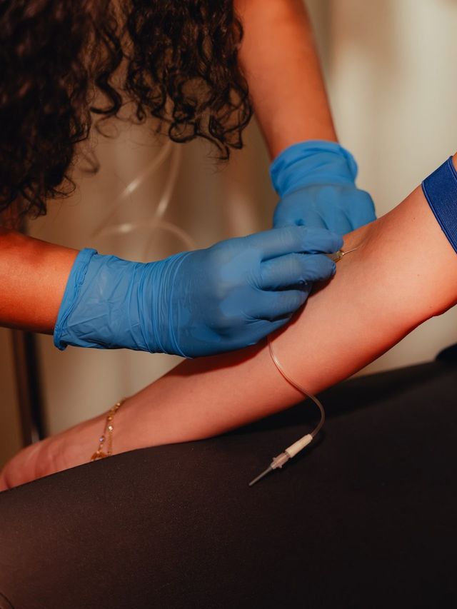 Blood draw: two hands in blue gloves at the arm, above it the tourniquet