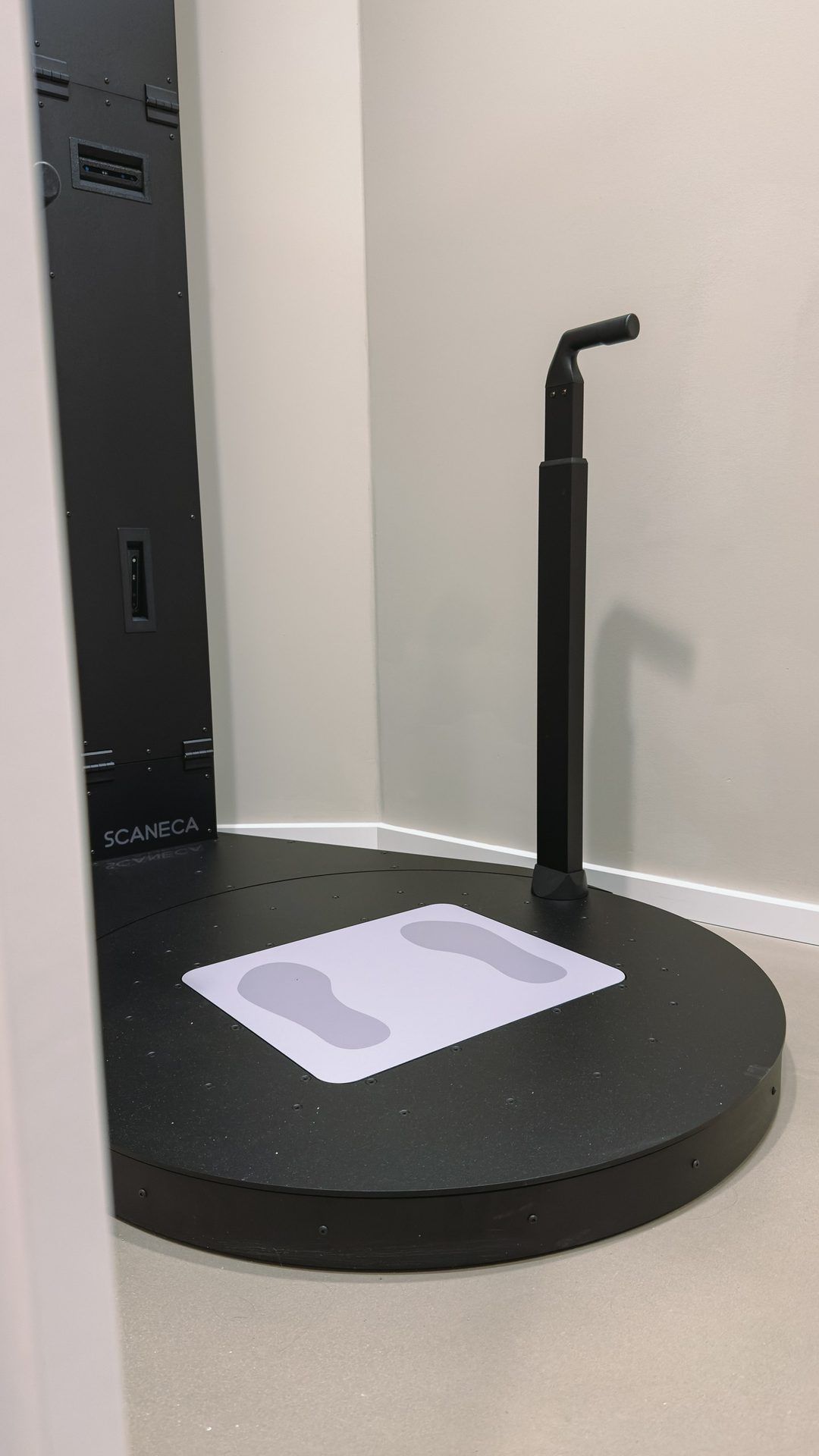 3D body scanner: a round black platform with footprints and a handle against pale walls