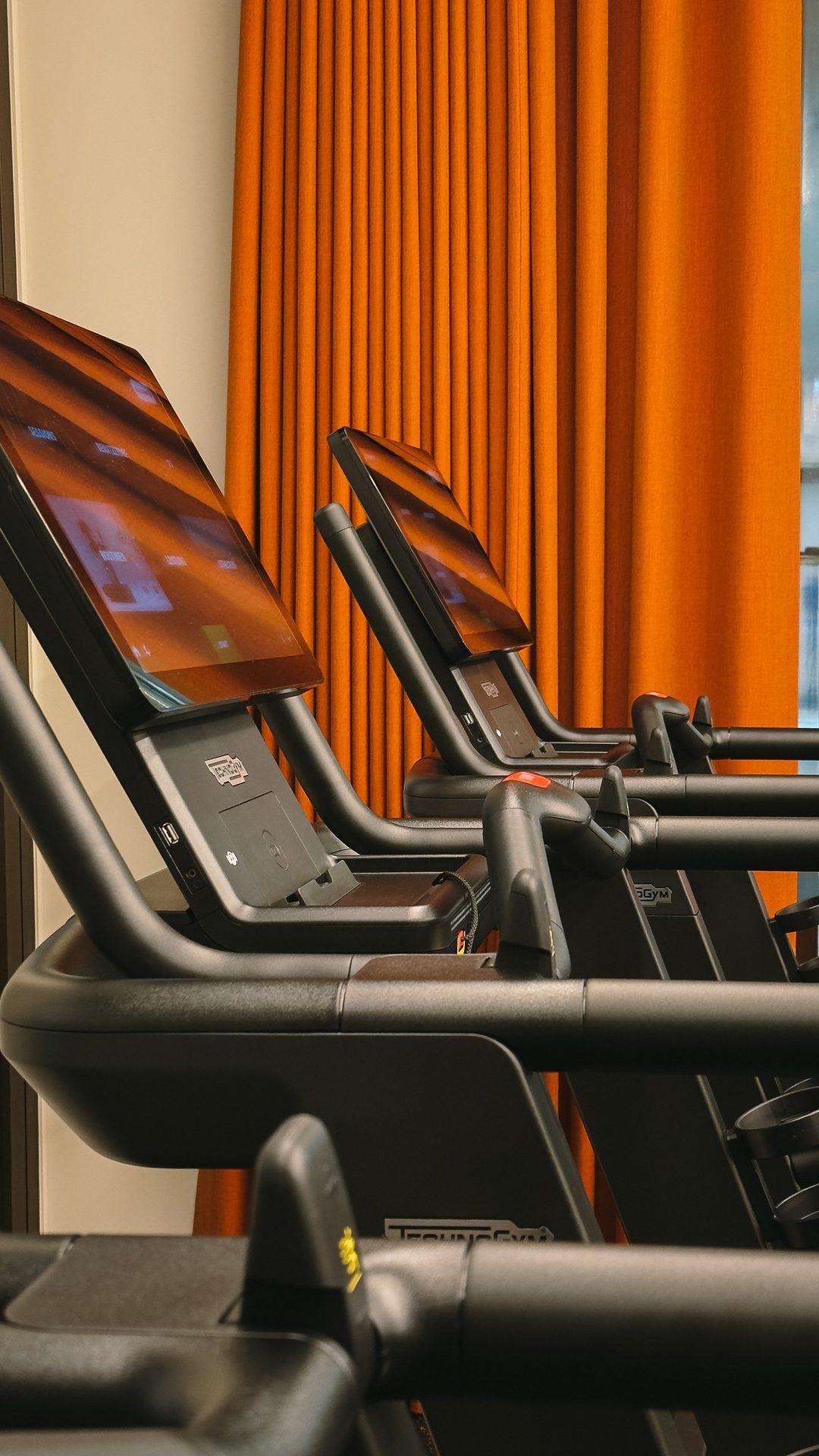 Cardio machines with screens in a row in front of a rust-red curtain