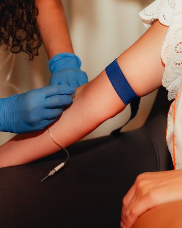Blood draw: gloved hands at an arm with a tourniquet