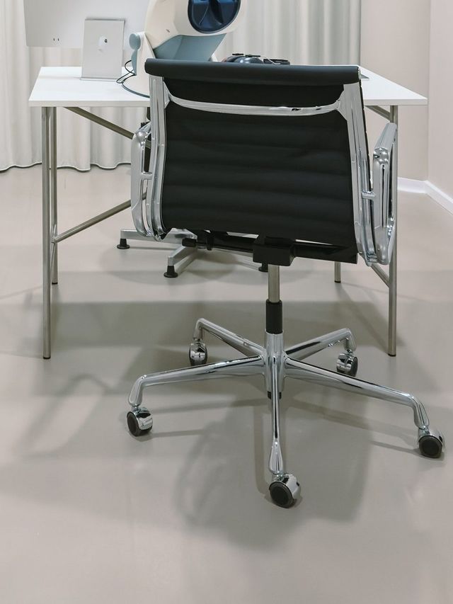 Office chair at a white desk in the examination room, a screen and the vision testing device on the desk, a light curtain behind