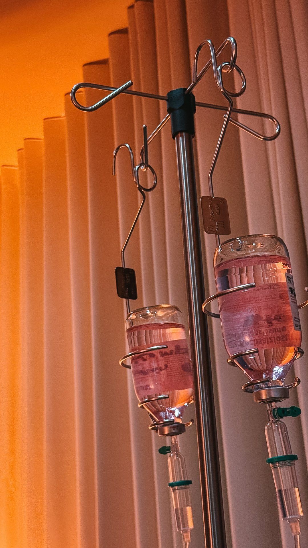 Two infusion bottles on a drip stand in front of an orange curtain