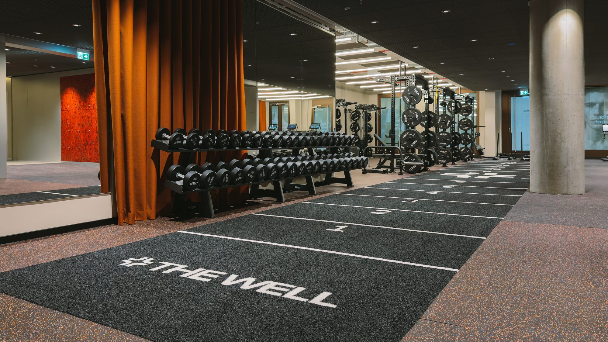 Gym with dumbbells and a sled track marked THE WELL, a rust curtain at the side
