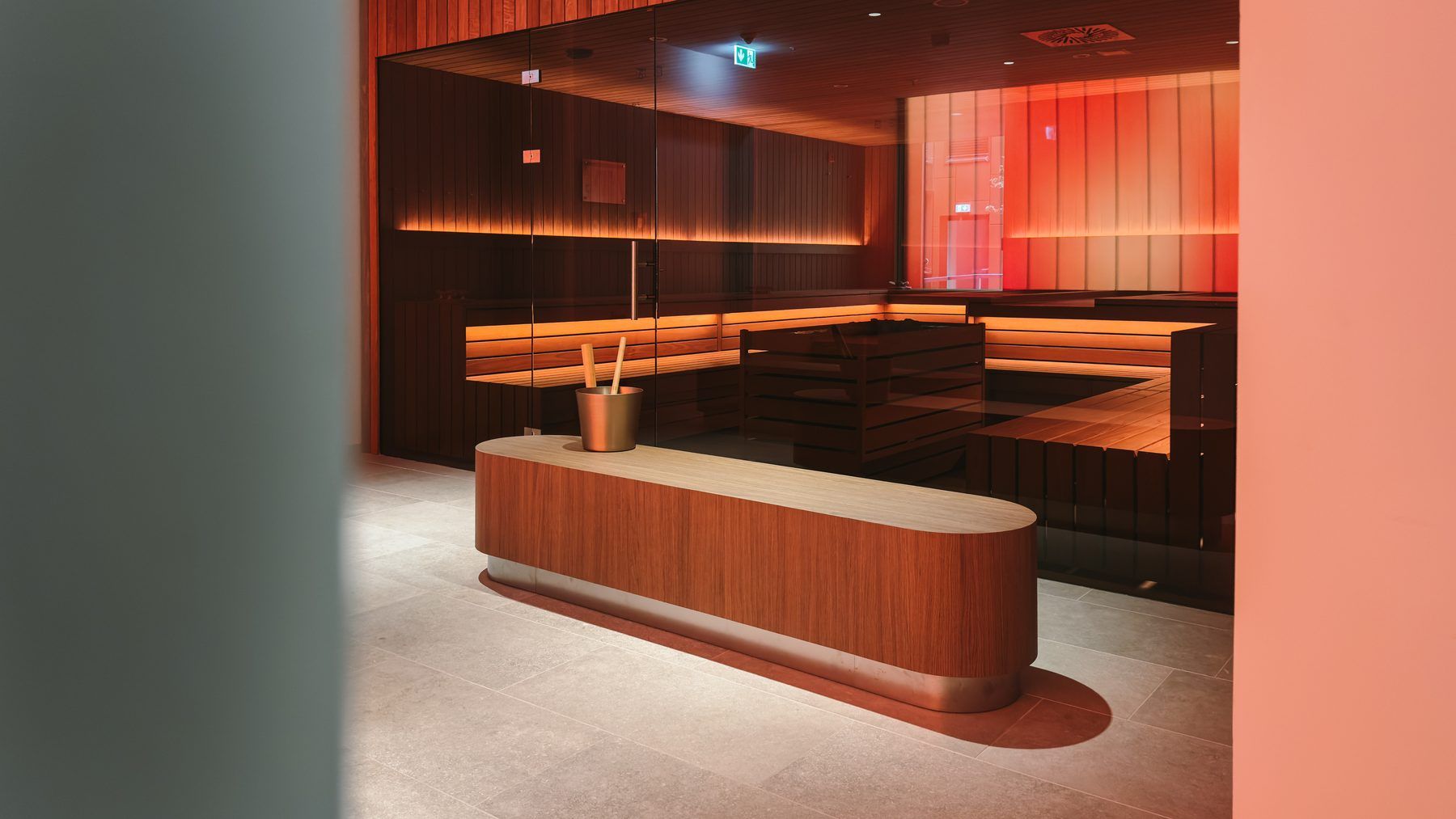 Sauna with wooden benches behind glass, a rounded wooden bench in front