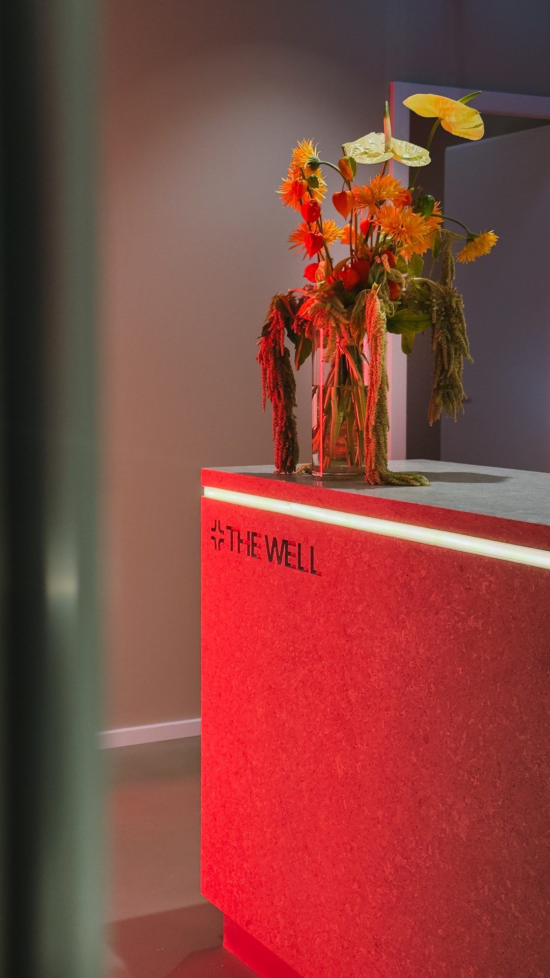 Reception desk with the THE WELL logo in red light, a vase of orange flowers on top