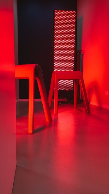 Red light therapy room: a tall LED panel with two chairs in front of it, everything in red light