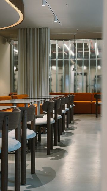 Restaurant with long rows of tables and wooden chairs, orange benches and a ribbed glass wall at the back